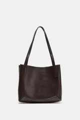 Bolso de hombro tipo shopper de cuero sintético color marrón oscuro, con pespuntes decorativos en el cuerpo y asas delgadas. Cierre principal con botón imantado y bolsillo interior con cremallera.