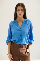 Camisa celeste con escote en V, mangas 3/4 abullonadas y bordado marrón en hombros y mangas. Cierre frontal con botones.