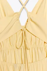 Vestido midi amarillo de tejido fluido con escote pico y tirantes finos cruzados en la espalda ajustables con lazada. Tiene detalle de elásticos bajo el pecho.