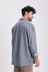 Sobrecamisa de hombre de jean, color azul, con patrón de rayas verticales finas. Presenta cuello camisero, bolsillos frontales con tapa y botones oscuros. Se lleva abierta sobre una remera blanca.