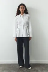 Camisa blanca de cuello solapa y manga larga. Detalle de pliegues con botones. Cierre frontal con botones.
