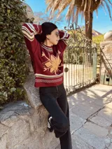 Sweater tejido color borgoña con diseño de copo de nieve en el frente y bordes con motivos geométricos en tonos beige, blanco y marrón.