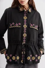 Campera negra de algodón con bordados de flores y lentejuelas. Tiene corte recto, ajuste interno en la cintura, bolsillos con solapa y cierre frontal.