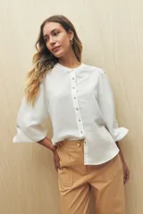 Camisa color crema a rayas verticales finas, de cuello mao, mangas 3/4 abullonadas con elástico en los puños y cierre frontal con botones de nácar.