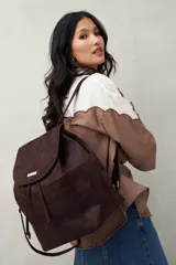 Mochila marrón de símil gamuza con diseño minimalista, solapa con cierre magnético, cordón ajustable, bolsillos laterales y acabado texturizado tipo reptil.