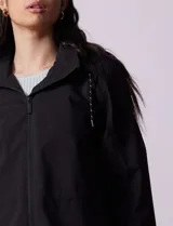 Gabardina negra impermeable con capucha desmontable, cierre central con cremallera y botones a presión, bolsillos delanteros y forro interno.
