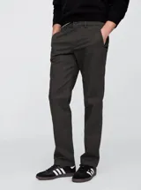 Pantalón de vestir color verde oscuro, de corte recto, con bolsillos laterales y traseros. Se ajusta a la cintura con cinturón de cuero marrón.