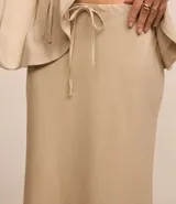 Conjunto color beige compuesto por una falda midi de lino y viscosa con lazo en la cintura y un chaleco sin mangas con botones. Incluye un bolso tote beige.