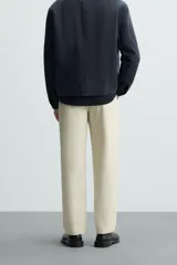 Pantalón chino color beige, corte recto, con bolsillos laterales y traseros. Cierre frontal con cremallera y botón.