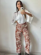 Pantalón de tela color terracota con estampado de hojas y flores en color blanco.