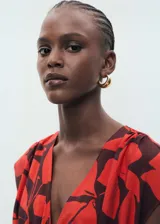 Vestido largo de viscosa y poliamida, estampado con hojas grandes en rojo y marrón oscuro. Presenta cuello en V, mangas cortas tipo mariposa y un panel fruncido ajustable con cordón en la cintura.