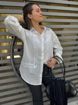 Camisa blanca de mangas largas con detalles de encaje en el frente, cuello y puños.