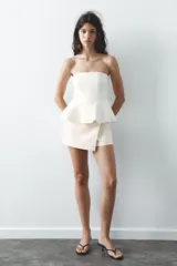 Falda pantalón corta color crudo, de tiro medio y cintura asimétrica cruzada.