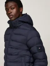 Campera Tommy Hilfiger acolchada color azul marino, con capucha fija ajustable con cordón, cierre de cremallera frontal, dos bolsillos laterales y parche engomado con el logo de la marca en la manga.