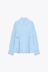 Camisa celeste de corte holgado, con cuello solapa, manga larga y cierre frontal con botones. Presenta detalle de cintura ajustable con botones.