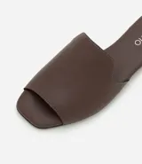 Sandalia plana de mujer color blanco hueso, con tira única ancha y puntera cuadrada abierta. Posee un taco bajo y suela de goma marrón.