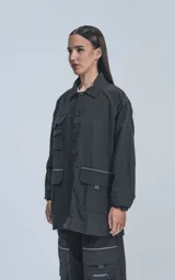 Campera negra oversize con broches en el delantero, forrada con red, múltiples bolsillos con detalles réflex y puños elásticos.