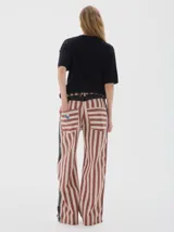 Pantalón de jean de tiro alto, pierna ancha y recta, con estampado de rayas verticales en tonos rojo óxido y beige claro. Presenta un panel lateral oscuro con textura de estampado sutil.