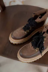 Botas de caña baja color marrón con cordones negros, suela track color beige y detalles en cuero.