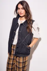 Chaleco oversize de denim negro con costuras en hilo ocre, cuello camisero, cierre frontal con botones y bolsillos delanteros.