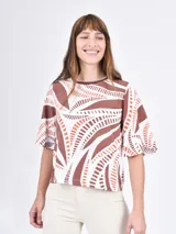 Blusa estampada con motivos geométricos en tonos marrón, naranja y blanco, de corte recto y mangas cortas abullonadas.