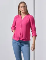 Blusa blanca de gasa marca Zac & Rachel, con cuello a la base, escote en V, abertura central con botones, bolsillo aplicado en el pecho y mangas largas regulables con presilla y botón. Tiene terminación opcional de nudo en el ruedo.