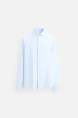 Camisa celeste a rayas verticales blancas, de corte recto, con cuello italiano abierto, manga larga con puños abotonados y cierre frontal con botones.