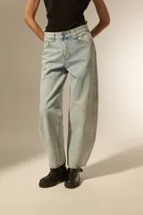 Pantalón de jean negro de corte ancho y tiro bajo, con detalles de tachas metálicas en los bolsillos delanteros y a lo largo de las costuras laterales.