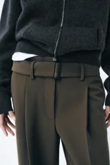 Pantalón de tiro medio color verde oliva, con cintura con trabillas, bolsillos laterales ocultos, cinturón ajustable con hebilla metálica, pinzas delanteras y cierre frontal con cremallera, botón y gancho metálico.