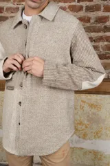 Camisa de hombre estilo leñadora con diseño patchwork en tonos beige y marrón. Presenta coderas, cartera americana y bolsillo ojal en el delantero. Confeccionada en lana fina sin teñir.