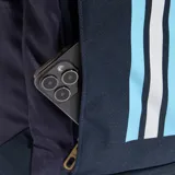Mochila deportiva Adidas, color azul marino oscuro, con tres franjas verticales en celeste claro, blanco y celeste, y logo de Adidas en dorado. Presenta correas ajustables y detalles en celeste claro.