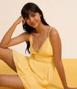 Vestido corto negro de viscosa certificada, con escote en V ribeteado con encaje, breteles finos y cuerpo con frunces horizontales. La falda tiene un volante con detalle de encaje en el ruedo.