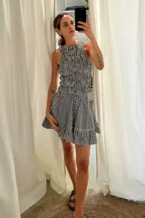 Vestido corto color marrón oscuro, sin mangas y con escote recto. Presenta un cuerpo fruncido con elástico y una falda corta con volados en el ruedo.