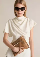 Blusa color blanco hueso con textura, de manga corta, tejido fluido y ligero. Presenta cuello alto envolvente, silueta slim y cierre de cremallera en la parte posterior.