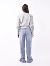 Saco azul de tejido de punto con botones dorados, escote en V y mangas largas con diseño trenzado.