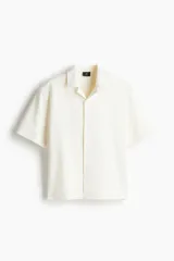 Camisa de manga corta color crema, de corte holgado, con cuello resort y cierre frontal con botones.