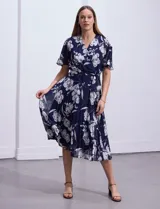 Vestido largo de gasa estampada con flores blancas sobre fondo azul marino, marca Sandra Darren. Tiene escote en V cruzado, cintura elastizada con lazo de ajuste, falda plisada y forro interno a tono.