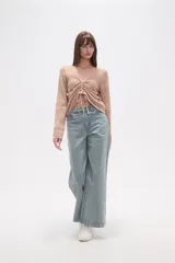 Sweater de poliéster color beige, con cuello en V, manga larga y frunces ajustables en el frente. Presenta un diseño de tejido calado.