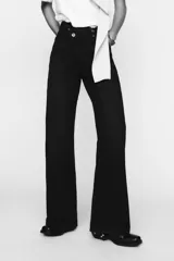 Pantalón de jean celeste de tiro alto, corte wide leg y largo hasta el tobillo. Presenta un diseño asimétrico en la cintura con cierre frontal cruzado con cremallera y botones metálicos.