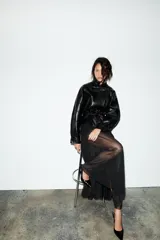 Cazadora negra de efecto piel, con cuello solapa y manga larga acabada en puño. Tiene bolsillos de vivo en delantero, cinturón lazada en mismo material y bajo acabado peplum. El cierre frontal es con cremallera.