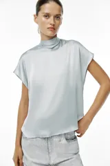 Blusa color crudo de tejido satinado, con cuello subido, manga sisa y cierre en la espalda con lazada y botones.