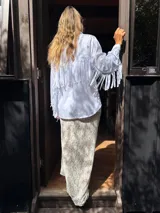 Camisa blanca de mangas largas con flecos en la espalda y en las mangas.