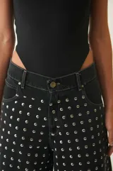 Bermuda de denim negro con tachas redondas plateadas, tiro bajo, cuatro bolsillos, pasacintos y cierre con botón metálico.