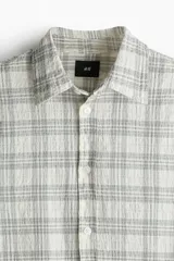 Camisa blanca con diseño a cuadros grises, de corte holgado, manga larga y cuello inglés.