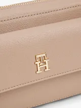 Bandolera Tommy Hilfiger color beige con correa ajustable y removible, compartimento principal con cierre de cremallera y logo monograma TH en la parte delantera.