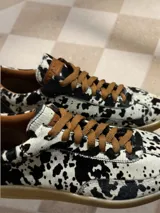 Zapatillas bajas con estampado animal print de vaca en blanco y negro, con cordones marrones y suela color caramelo.