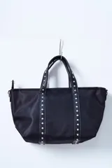 Bolso negro tipo tote bag con apliques de tachas plateadas en las asas y en los laterales.