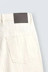 Pantalón de jean color crudo con textura de rayas verticales, corte relaxed fit, tiro medio, cinco bolsillos y cierre frontal con cremallera y botón.