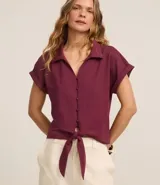 Blusa color borgoña de viscosa texturizada, con cuello, abotonada al frente, mangas cortas con dobladillo y lazo en la cintura.