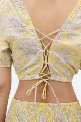 Blusa cropped de algodón color amarillo con estampado paisley en tonos grises. Tiene escote cuadrado elástico, mangas cortas con puños ajustados, espalda descubierta y tiras para atar.